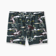 Pair of hunter green slim fit boxers with trees and men riding horses printed on sitting against light grey background.
