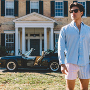 Man standing in front of large house wearing blue dress shirt and pastel stripe slim fit boxers.