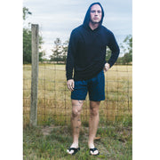 Man wearing black hoodie and midnight leopard lounge shorts standing next to fence in a field.