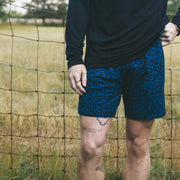 Close up of man wearing midnight leopard lounge shorts by a fence in a field.
