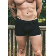 Man standing shirtless with hands behind back wearing black boxer brief.