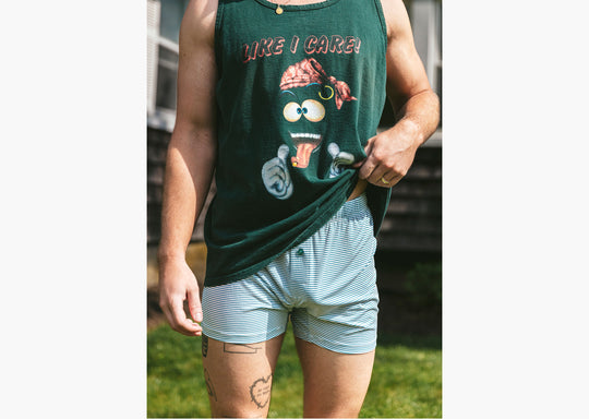 Close up shot of man wearing sleeveless black shirt and green striped slim fit boxers standing outside in front of a house.