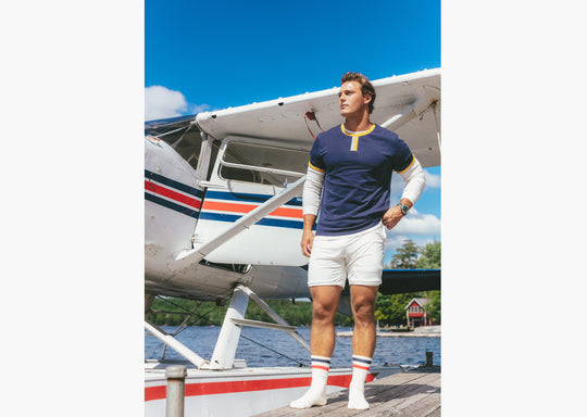 Man standing in front of plane wearing Navy vintage ringer and cream lounge shorts