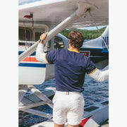 Back shot of man standing in front of plane wearing Navy vintage ringer and cream lounge shorts