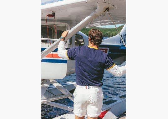Back shot of man standing in front of plane wearing Navy vintage ringer and cream lounge shorts