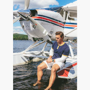 Man sitting on dock in front of plane wearing Navy vintage ringer and cream lounge shorts