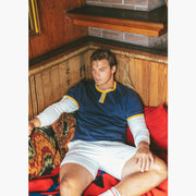 Man sitting inside on couch wearing Navy vintage ringer and cream lounge shorts