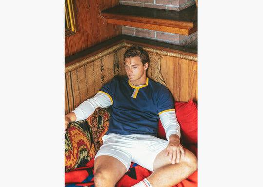 Man sitting inside on couch wearing Navy vintage ringer and cream lounge shorts