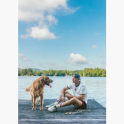 Man sitting on lake dock wearing white vintage ringer tee shirt and burgundy lounge shorts.