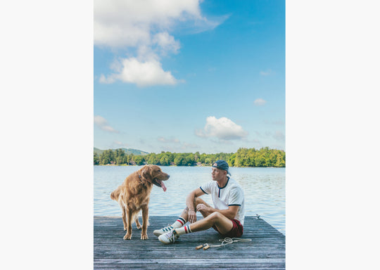 Man sitting on lake dock wearing white vintage ringer tee shirt and burgundy lounge shorts.