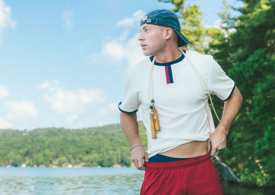 Man standing on lake dock wearing white vintage ringer tee shirt and burgundy lounge shorts.