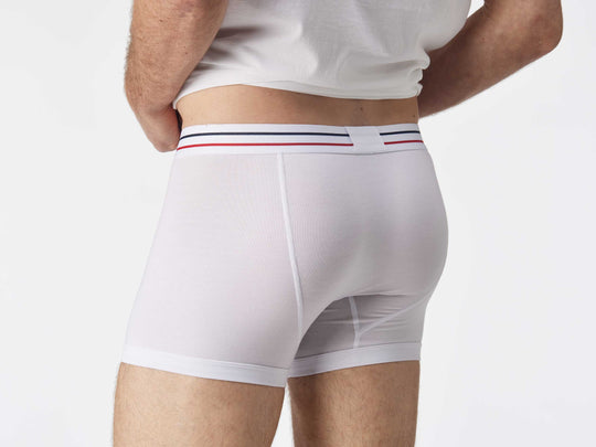 Close up back view of man wearing white boxer brief with blue and red stripe on label.