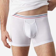 Close up front view of man wearing white boxer brief with blue and red stripe on label.