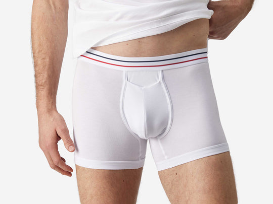 Close up front view of man wearing white boxer brief with blue and red stripe on label.