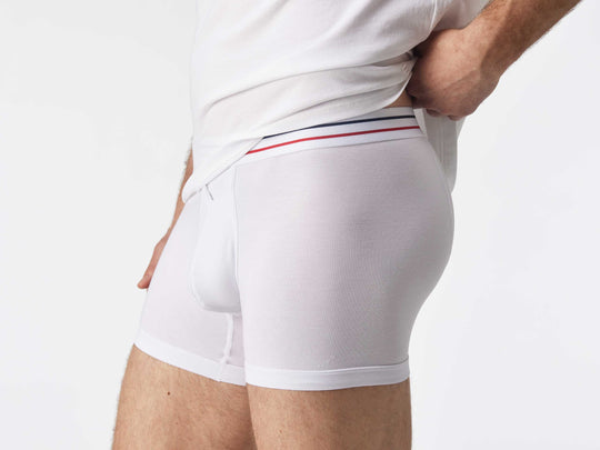 Close up side view of man wearing white boxer brief with blue and red stripe on label.