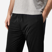 Close up front view of man wearing black lounge pants with hand in pocket.