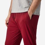 Close up side view of man wearing burgundy lounge pants with hand in pocket.