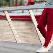 Man wearing burgundy lounge pants leaning against a railing with river in the background.