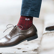 Man wearing brown dress shoes with red plaid monogram socks on city street.