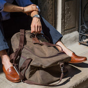 Man sitting on the steps with duffle bag and loafers wearing no-shows.