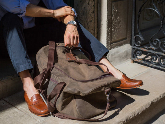 Man sitting on steps with duffle bag and loafers wearing no-show socks.