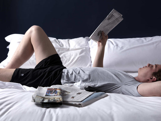 Man reading newspaper in bed wearing pocket lounge shorts.