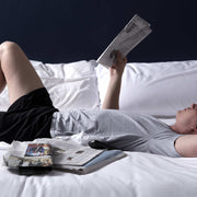 Man reading newspaper in bed wearing pocket lounge shorts.