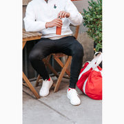 Man sitting at a cafe wearing black lounge shorts with red bag next to him.
