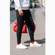 Man wearing black lounge shorts outside holding red bag.
