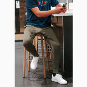 Man at a kitchen island wearing matte olive lounge pants checking his phone.