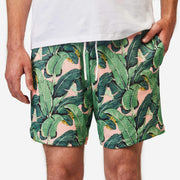 Close up front view of man wearing pink mesh lounge shorts with palm leafs printed in green.