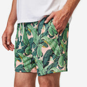 Close up front side view of man wearing pink mesh lounge shorts with palm leafs printed in green.