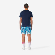 Full body back view of man wearing blue and white wave printed lounge shorts.