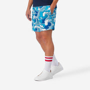 Close up side view of man wearing blue and white wave printed lounge shorts with hand in pocket.