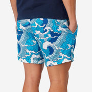 Close up back side view of man wearing blue and white wave printed lounge shorts with hand in pocket.