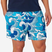 Close up front view of man wearing blue and white wave printed lounge shorts with hand in pocket.