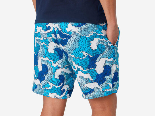 Close up back view of man wearing blue and white wave printed lounge shorts with hand in pocket.