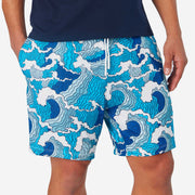 Close up front view of man wearing blue and white wave printed lounge shorts with hand in pocket.