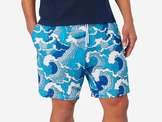 Close up front view of man wearing blue and white wave printed lounge shorts with hand in pocket.