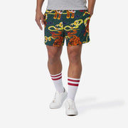 Front view of man wearing green lounge shorts with tiger and snake print with his hand in his pocket.